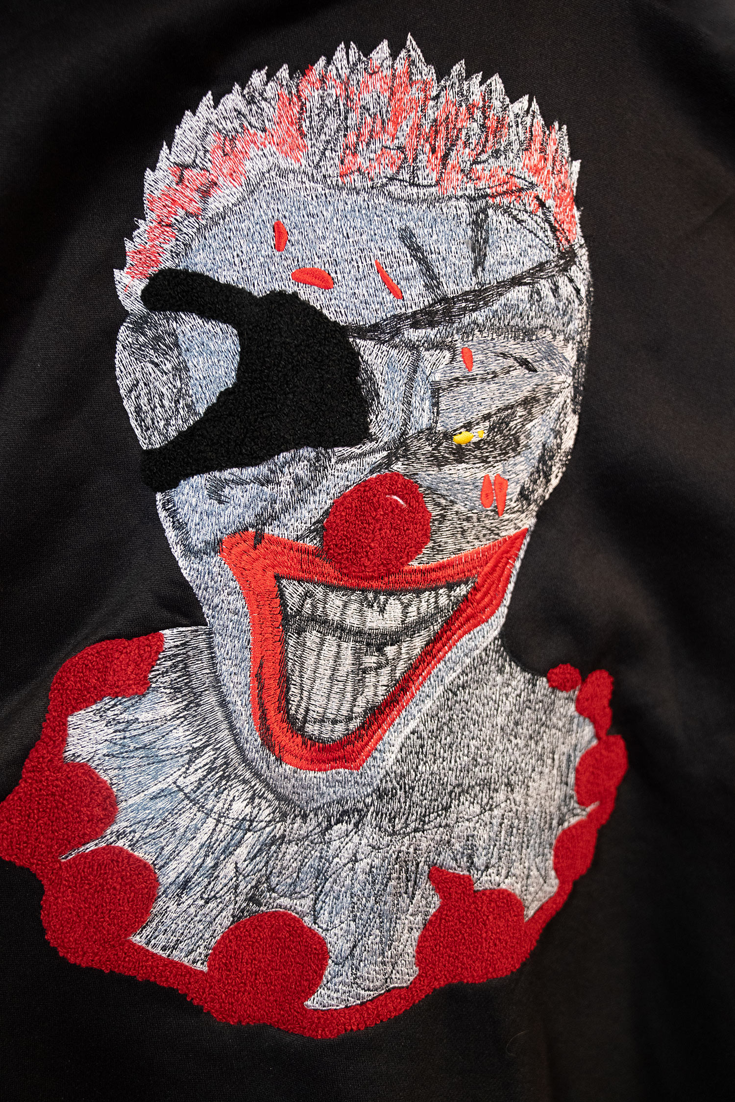 Abstract embroidered clown face on black fabric.